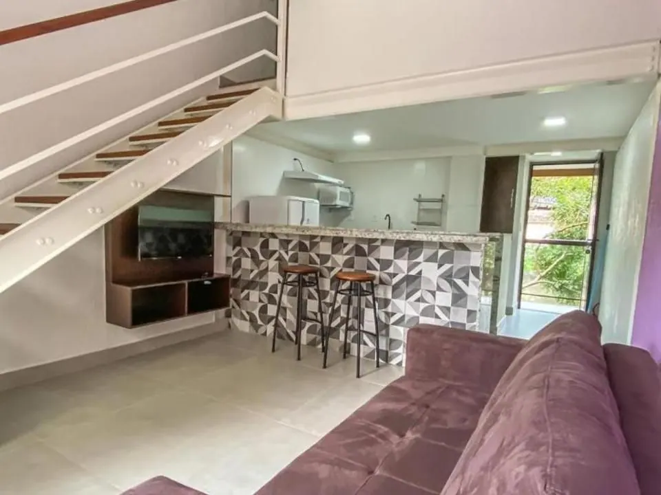 Sala do Flat Master do Bugio Flats com sofá-cama, escada para o mezanino, bancada americana e cozinha - flats na Vila do Abraão, Ilha Grande