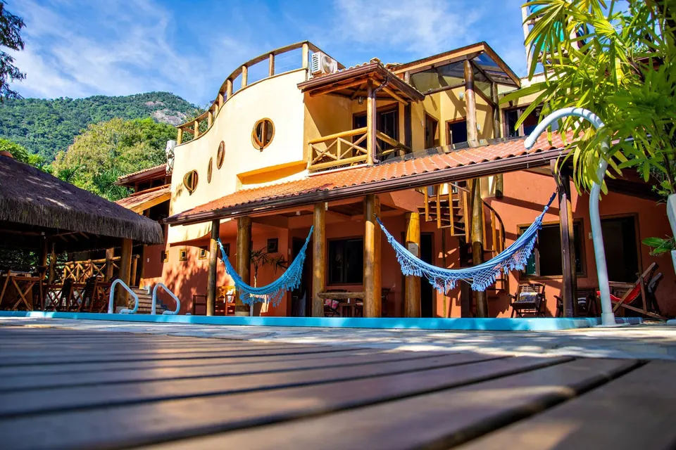 Fachada da Pousada Casa Bonita vista do deck da piscina, com varandas de madeira, redes e a mata ao fundo - pousada na Vila do Abraão, Ilha Grande
