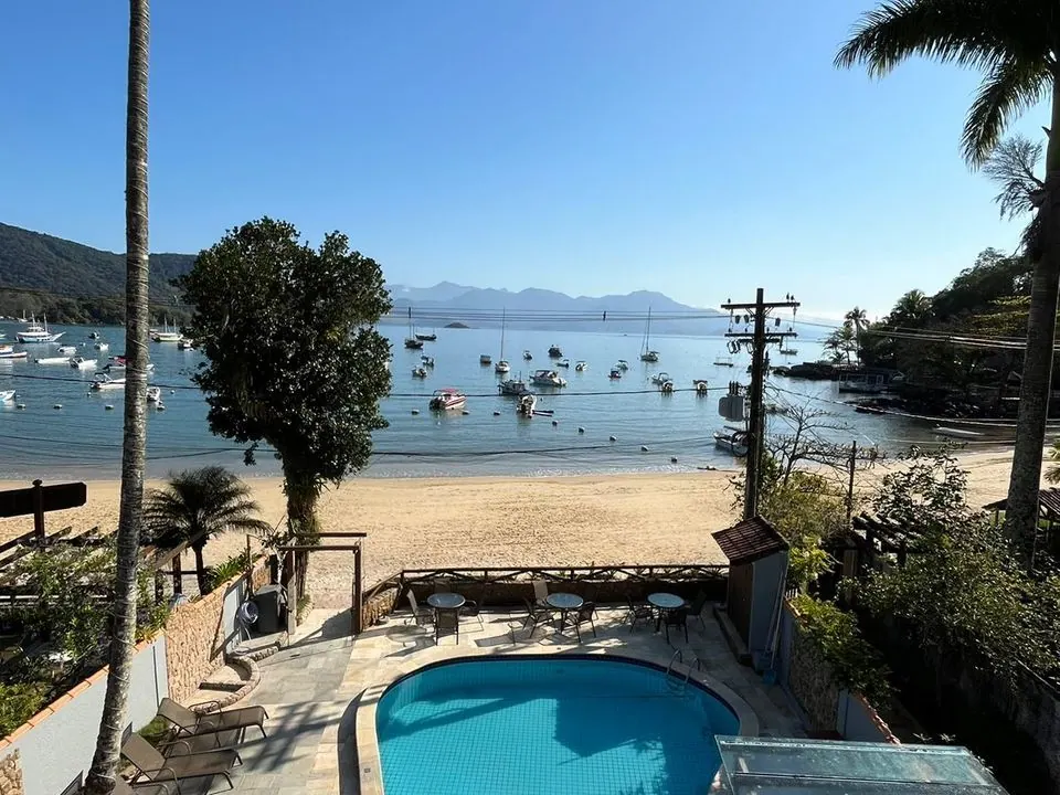 Piscina e deck da Pousada do Canto com a praia e o mar cheio de barcos à frente - pousada pé na areia na Vila do Abraão, Ilha Grande