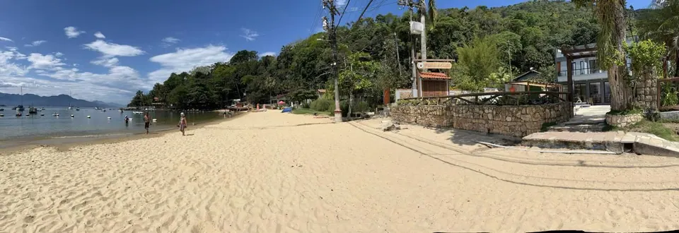 Praia de areia clara e mar calmo com barcos em frente à Pousada do Canto, na Vila do Abraão